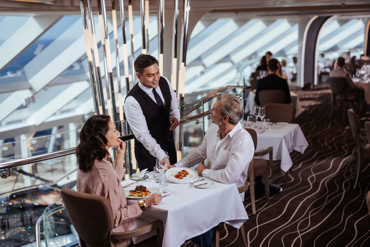 A waiter serves a couple at a dining table in the elegant MSC Yacht Club Restaurant onboard | MSC Cruises