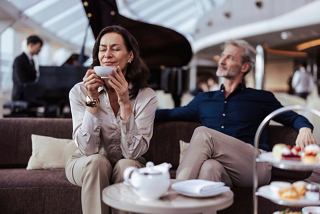 A couple enjoys afternoon tea in the elegant MSC Yacht Club Top Sail Lounge with live piano music in the background | MSC Cruises