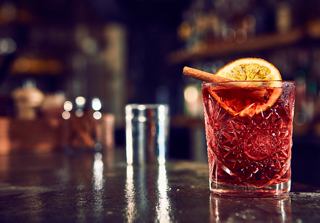 A refreshing cocktail garnished with an orange slice, set against a warm bar backdrop | MSC Cruises