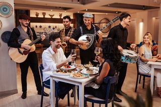 Una vivace scena di ristorante con ospiti che gustano cibo e vino, accompagnata da musica dal vivo | MSC Crociere