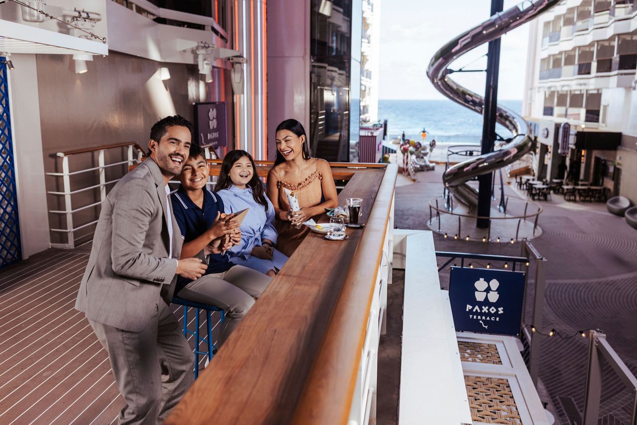 Las familias disfrutan de cenar juntas en un vibrante restaurante a bordo del MSC World America, con un tobogán acuático a la vista | MSC Cruceros