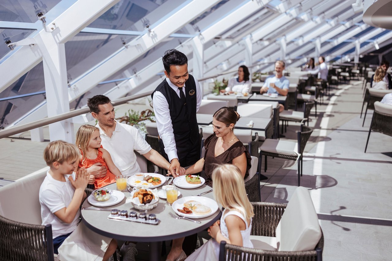 Une famille prend son petit-déjeuner ensemble dans le lumineux Top Sail Lounge, avec un personnel attentif leur servant de délicieux plats | MSC Cruises