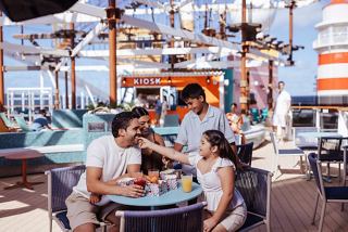 Eine Familie genießt gemeinsam eine Mahlzeit im The Harbour Bar & Bites, umgeben von einem sonnigen Himmel und lebendiger Atmosphäre | MSC Cruises