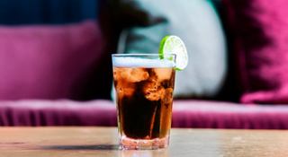 A refreshing glass of cola with ice and a lime wedge, set against a vibrant background | MSC Cruises