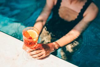 A woman holds a vibrant cocktail while relaxing by the pool on MSC Meraviglia | MSC Cruises
