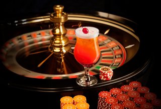A vibrant cocktail sits beside a roulette wheel and chips, inviting an exciting casino experience | MSC Cruises