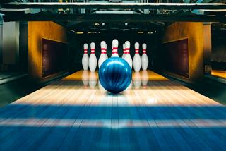 A blue bowling ball rolls towards a set of pins in a bowling alley | MSC Cruises