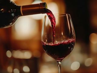 A glass being filled with red wine from a bottle in a warm dining setting | MSC Cruises