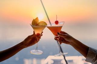 A couple toasts with cocktails against a sunset backdrop, celebrating unforgettable moments | MSC Cruises