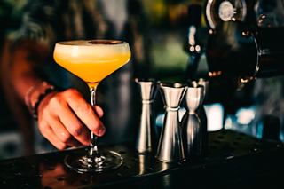 A hand holding a vibrant cocktail in a lively bar setting on the MSC Meraviglia | MSC Cruises