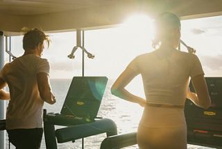 Two individuals engaged in a fitness workout on treadmills, enjoying sunlight in a vibrant onboard gym | MSC Cruises