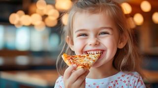 A joyful girl enjoying a slice of pizza in a warm dining atmosphere | MSC Cruises