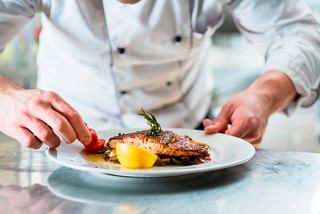 A chef expertly garnishing a salmon dish with tomatoes, showcasing culinary artistry on MSC Grandiosa | MSC Cruises
