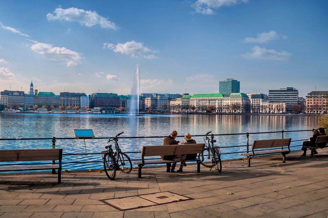 Menschen genießen einen sonnigen Tag am Binnenalstersee in Hamburg, während Segelboote sanft über das Wasser gleiten | MSC Cruises