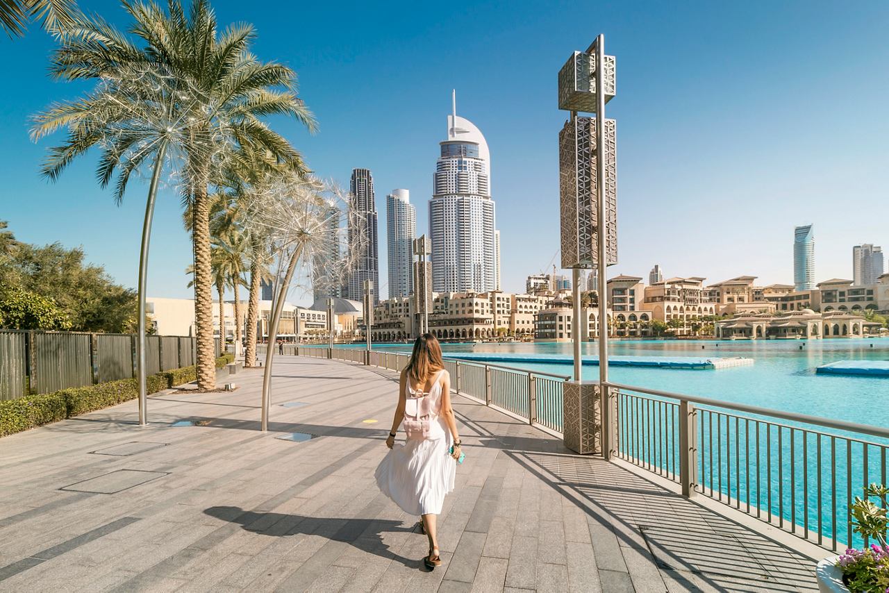 A woman strolls along a walkway near The Address Downtown, with palm trees and skyscrapers in the background | MSC Cruises