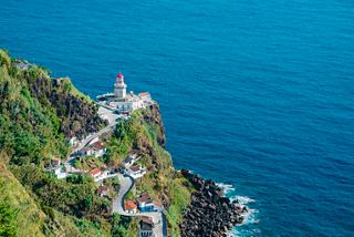 Una vista escénica de un faro en un acantilado con vistas al profundo mar azul en Ponta do Arnel, São Miguel, Portugal | MSC Cruceros