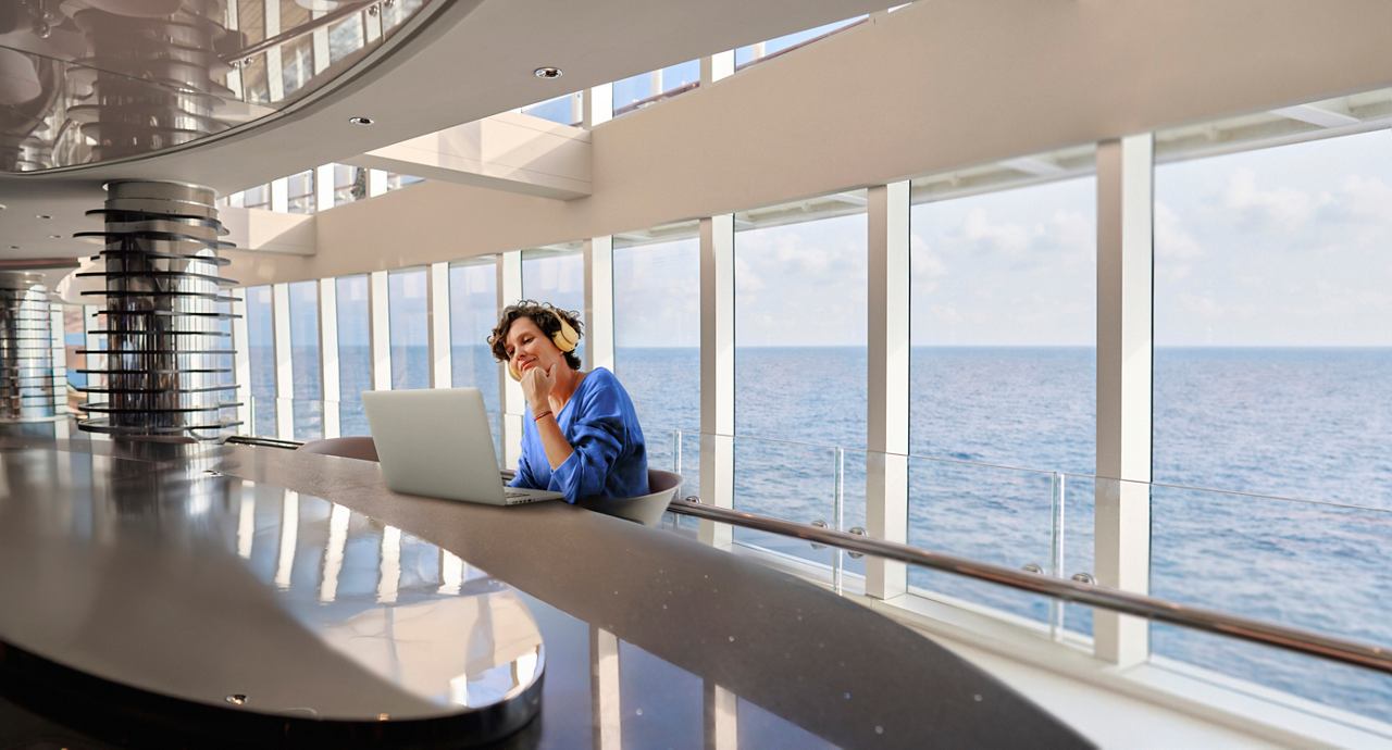 A woman works on a laptop in a bright room with a view of the sea | MSC Cruises