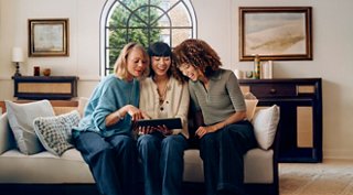 Three friends enjoy quality time together, looking at a tablet in a cozy home | MSC Cruises