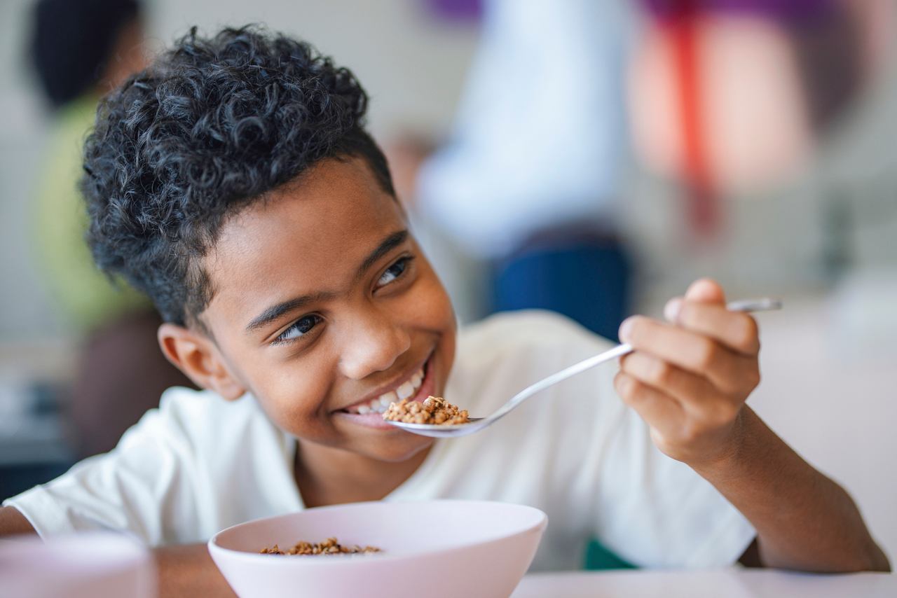 A happy child enjoys breakfast from a bowl, smiling with a spoon in hand | MSC Cruises