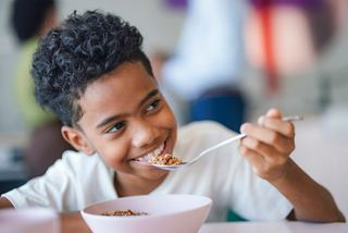 Un niño feliz disfruta de su desayuno en un tazón, sonriendo con una cuchara en la mano | MSC Cruceros