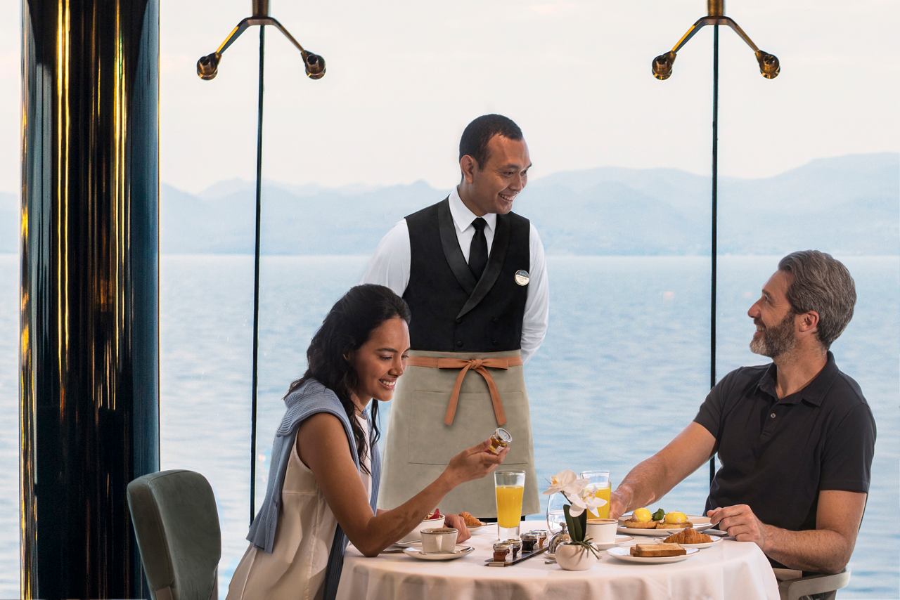 Un couple profite d'un petit-déjeuner souriant, servi par un serveur à bord. | MSC Croisières