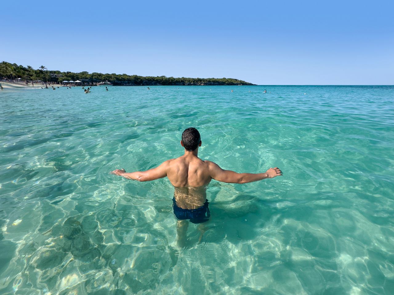 Hombre en agua cristalina, con los brazos extendidos en un paraíso tropical | MSC Cruceros