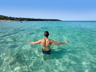Hombre en agua cristalina, con los brazos extendidos en un paraíso tropical | MSC Cruceros