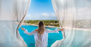 Frau blickt durch Fenster auf karibischen Strand und Vegetation | MSC Cruises