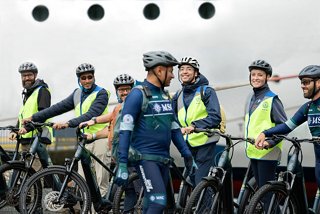 Crew on a bike tour by the sea with smiles, rocks, and fleet in the background | MSC Cruises