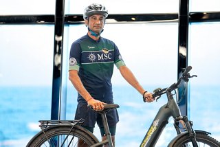 Happy MSC Euribia crew member on bike with sea and ship in the background | MSC Cruises