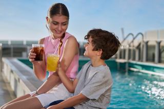 A teen and child enjoy soft drinks by the pool on a cruise ship with a bright sky above | MSC Cruises