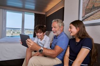 Family enjoys time together in a cabin with a tablet and sea view through the window | MSC Cruises