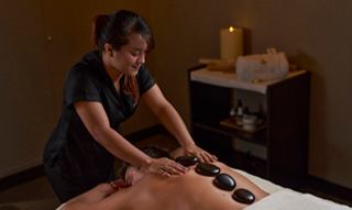 A massage therapist delivers a soothing hot stone massage in a tranquil spa setting | MSC Cruises