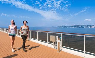 Two women enjoy a sunny day walking along a seaside path with a dog | MSC Cruises
