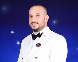 Captain in a white uniform, smiling against a starry background | MSC Cruises