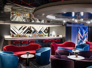 Un área de salón moderna y acogedora con asientos rojos y azules, perfecta para relajarse y socializar | MSC Cruceros
