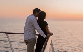 Ein Paar umarmt sich auf einem Kreuzfahrtbalkon und genießt den romantischen Sonnenuntergang über dem Ozean | MSC Cruises