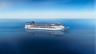 Ein majestätisches MSC Cruises Schiff gleitet durch ruhige blaue Gewässer unter einem klaren Himmel | MSC Cruises